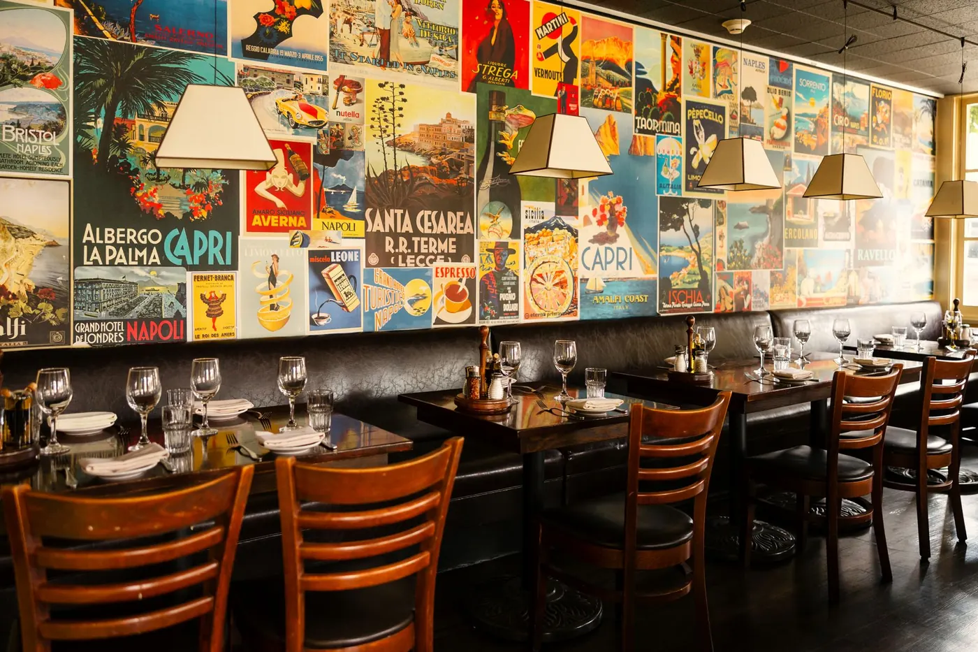 The Vesuvio dining room: wood tables set for dinner, yellow walls and a wall of vintage Italian travel posters