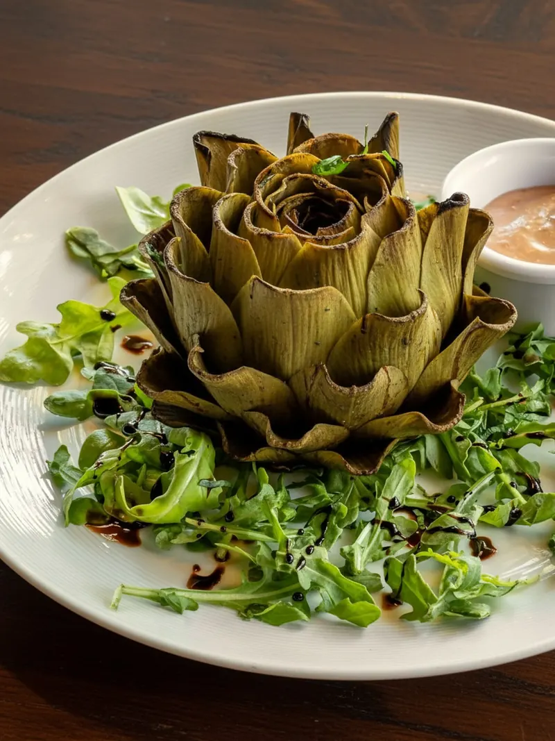 Grilled heirloom artichoke opened like a flower on arugula, with a cup of sauce
