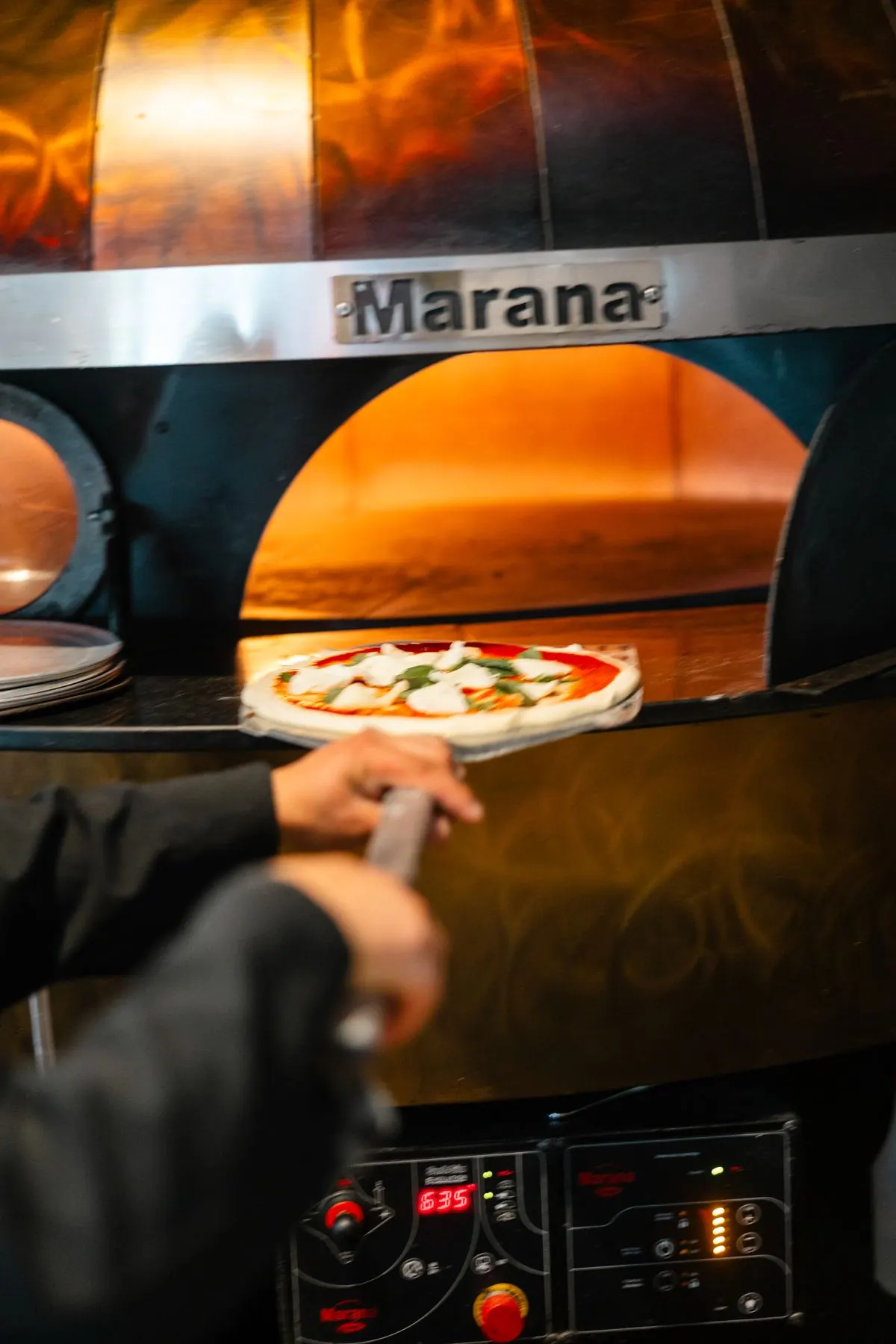 A pizza on the peel sliding into the flames of the wood-fired oven