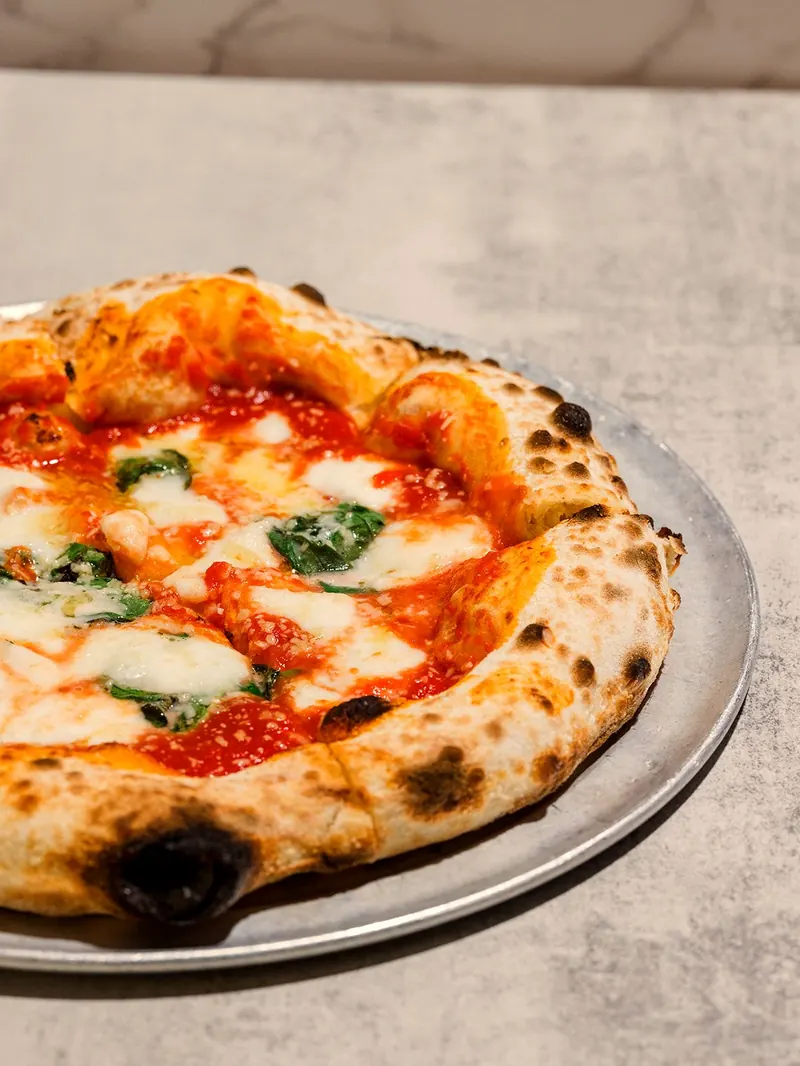Margherita pizza on a steel tray, leopard-spotted crust, basil and mozzarella