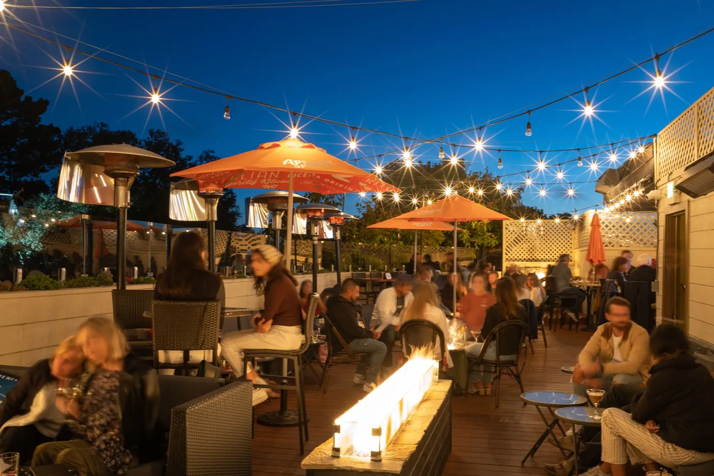 The Starlight Lounge on the Vesuvio rooftop at night: string lights, a fire pit, umbrellas and a full crowd
