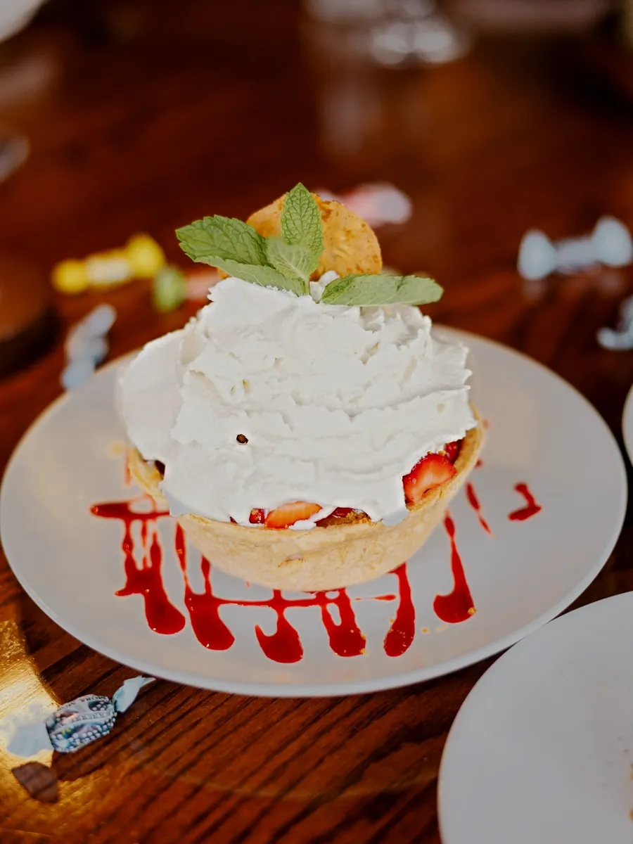 Strawberry creme pie, a crisp shell piled with whipped cream and mint, strawberry sauce on the plate