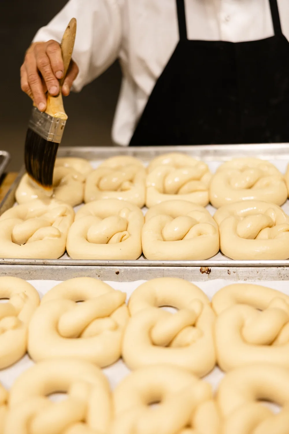 A baker's brush glazing rows of raw pretzels