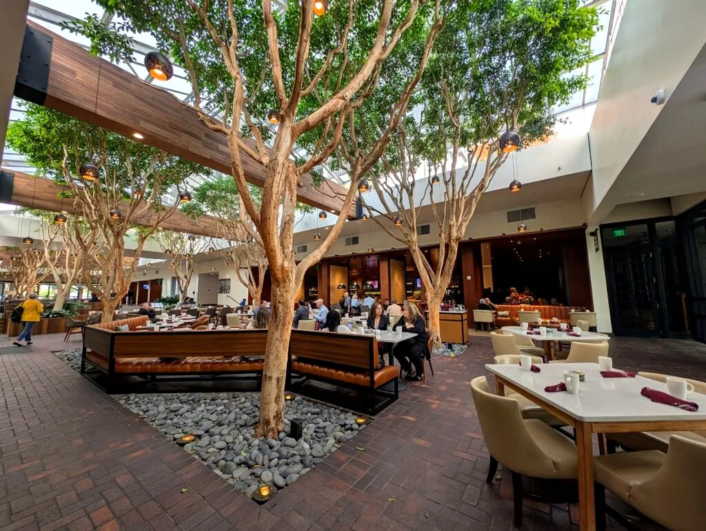 The skylit atrium lobby of Portola Hotel & Spa, with trees and hanging lights
