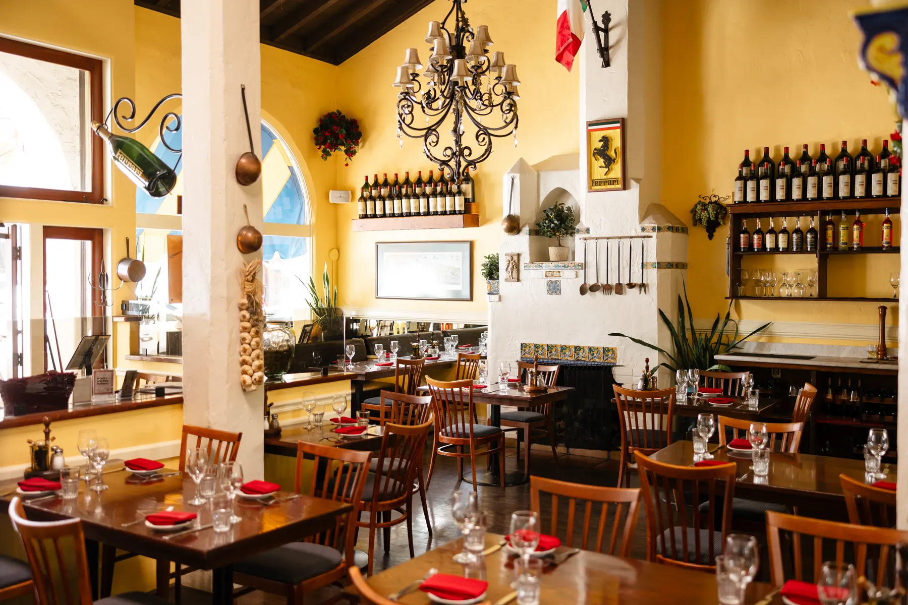 The Little Napoli dining room: yellow walls, framed photographs of Italy, a Ferrari banner and a chandelier over tables set for dinner