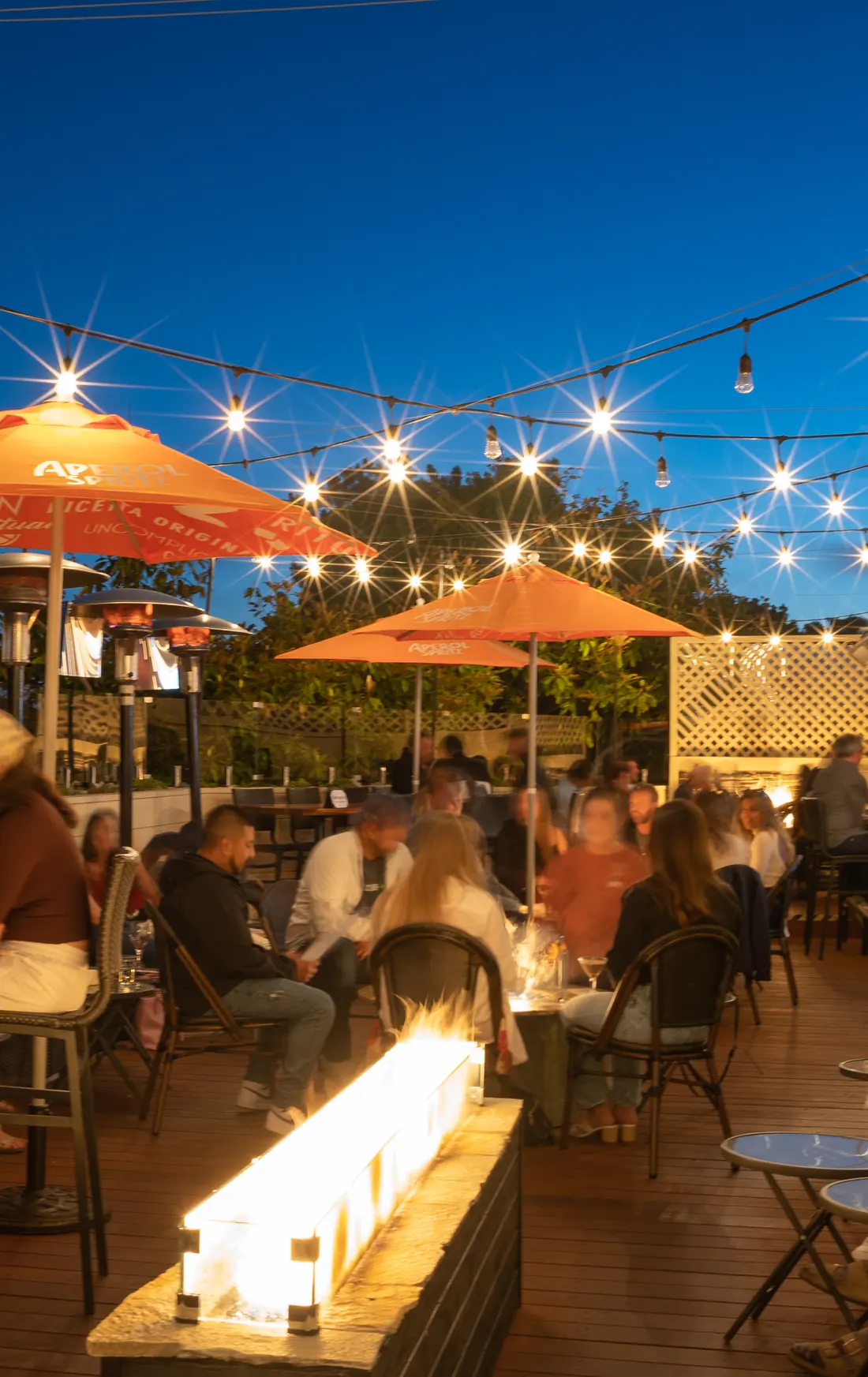 The Starlight Lounge on the Vesuvio rooftop at dusk: string lights, a fire trough and a full deck