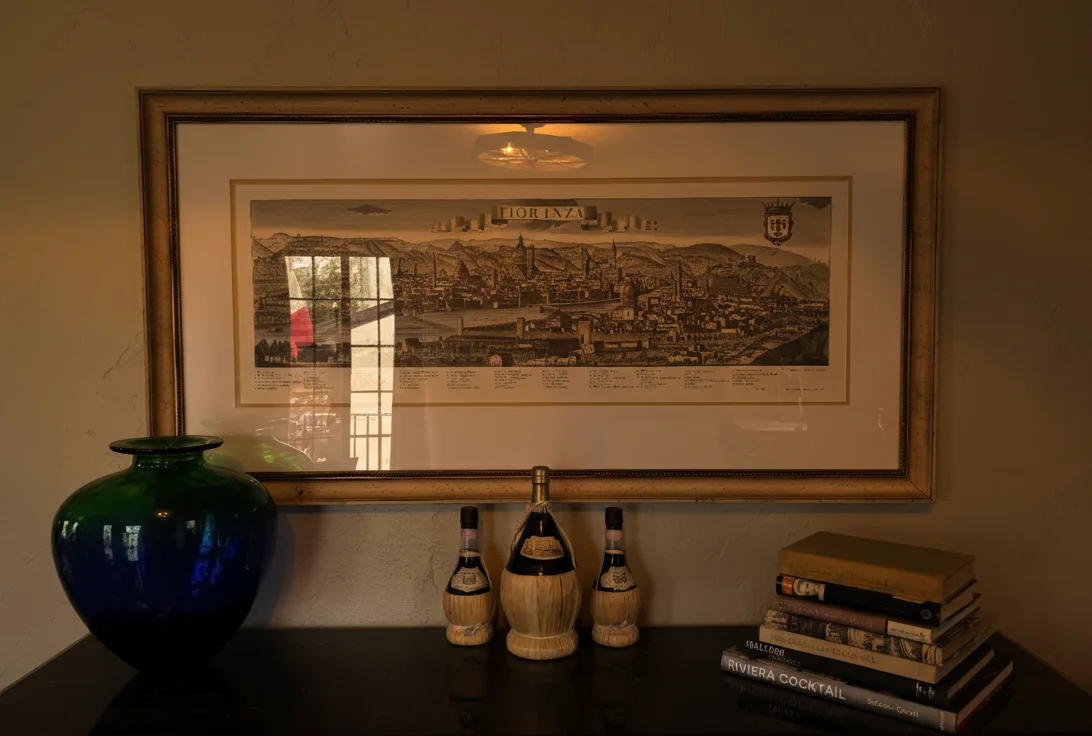 A framed panorama over a console in the La Dolce Vita room, with a blue vase, wine flasks and books